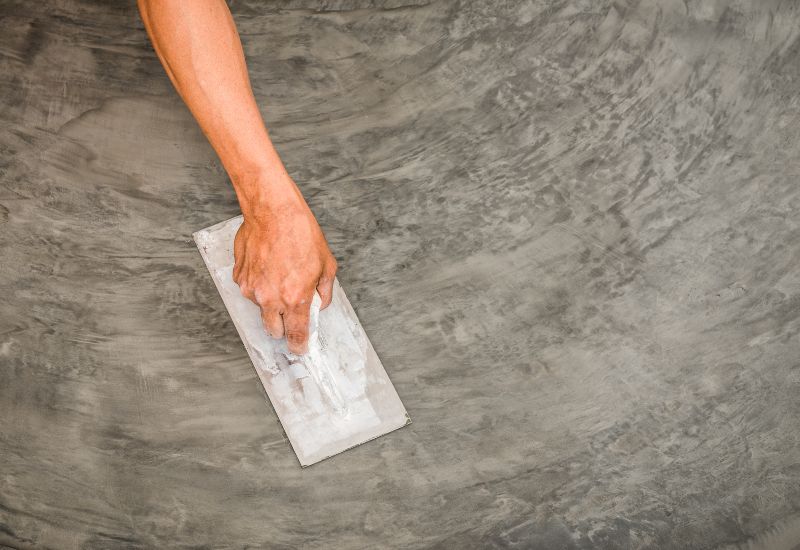 Close up of hand using steel trowel to finish wet concrete floor of polished concrete surface
